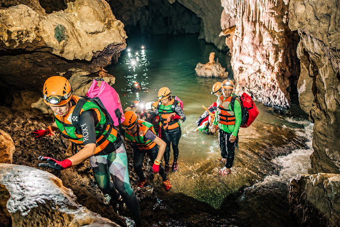 Adventurers wearing helmets and life jackets exploring a water-filled cave in Phong Nha