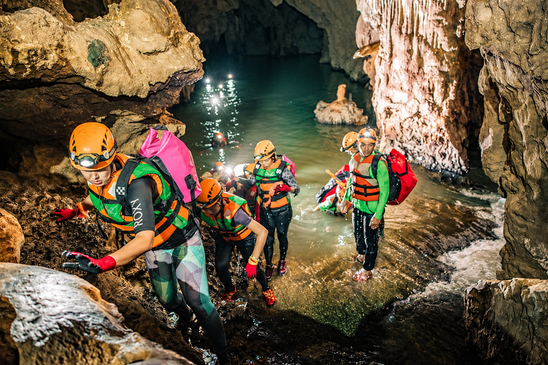 Adventurers wearing helmets and life jackets exploring a water-filled cave in Phong Nha